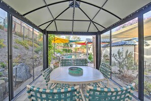Eine überdachte Terrasse mit einem runden Tisch und grün gestreiften Stühlen, umgeben von einem Metallzaun.