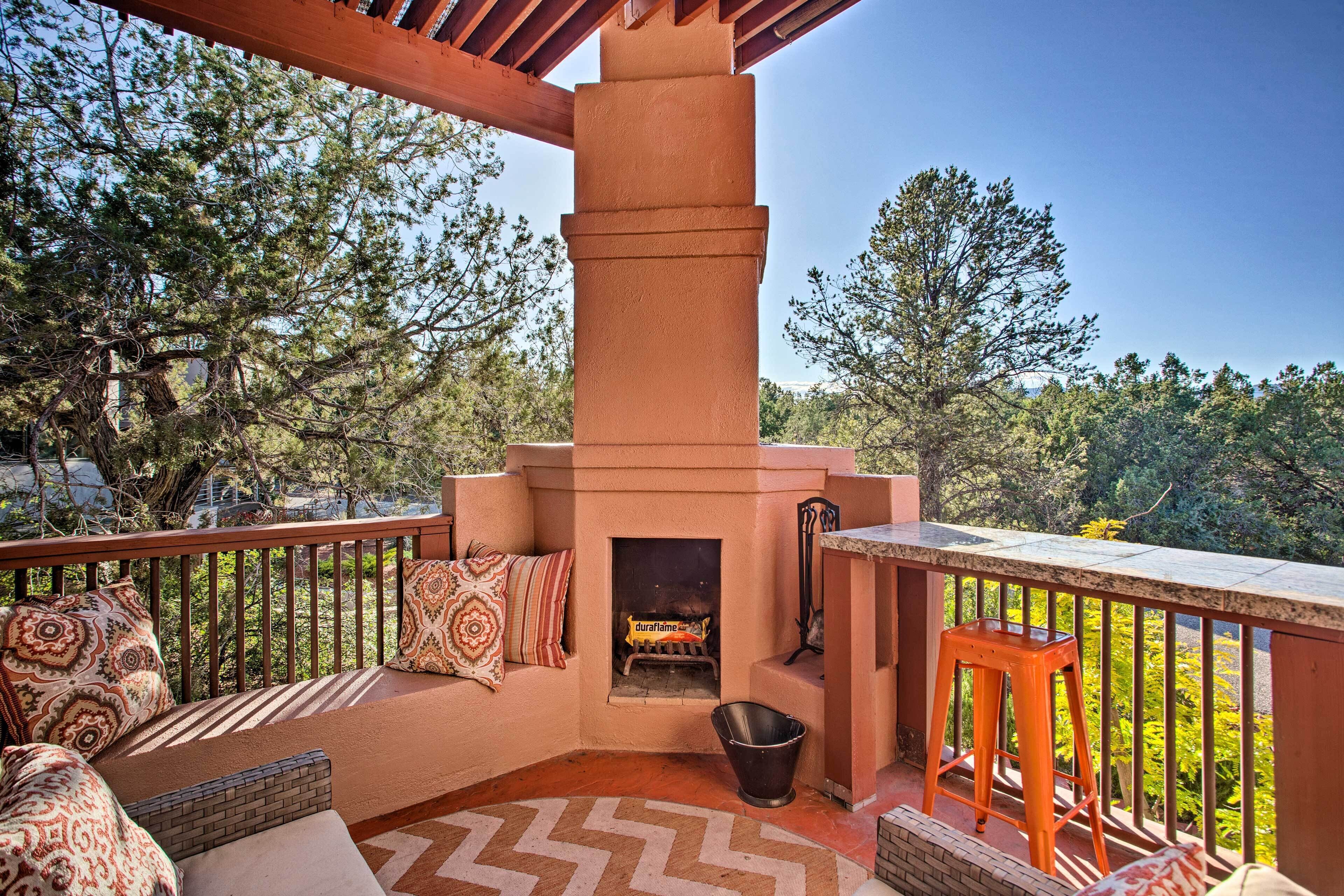 A cozy outdoor patio with a built-in fireplace, seating area, and a view of the surrounding trees.