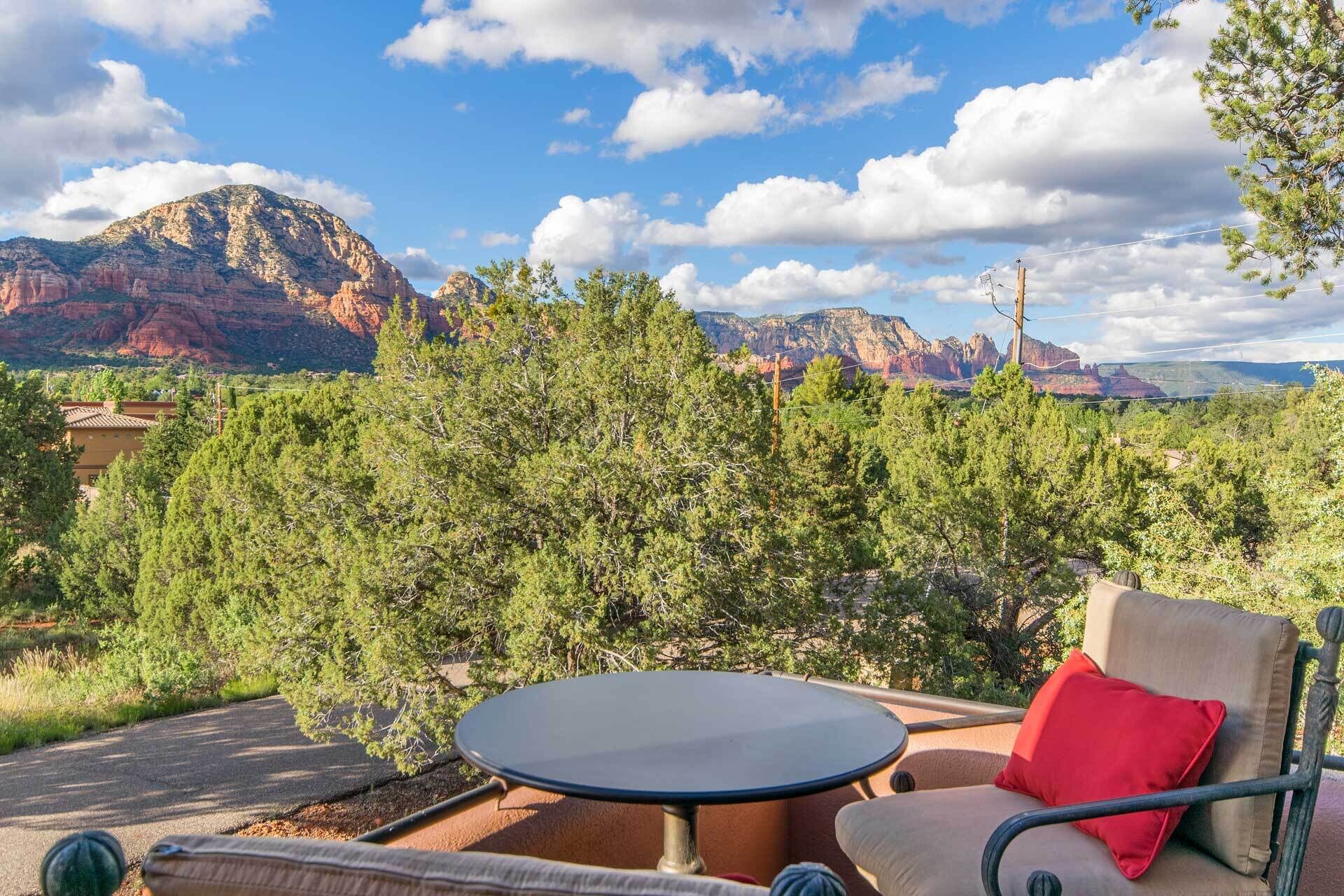 An outdoor seating area with a table and chairs, surrounded by trees and a view of red rock formations.