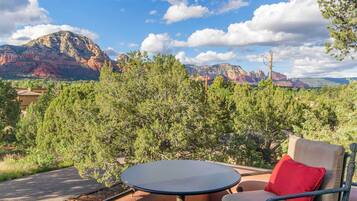 An outdoor seating area with a table and chairs, surrounded by trees and a view of red rock formations.