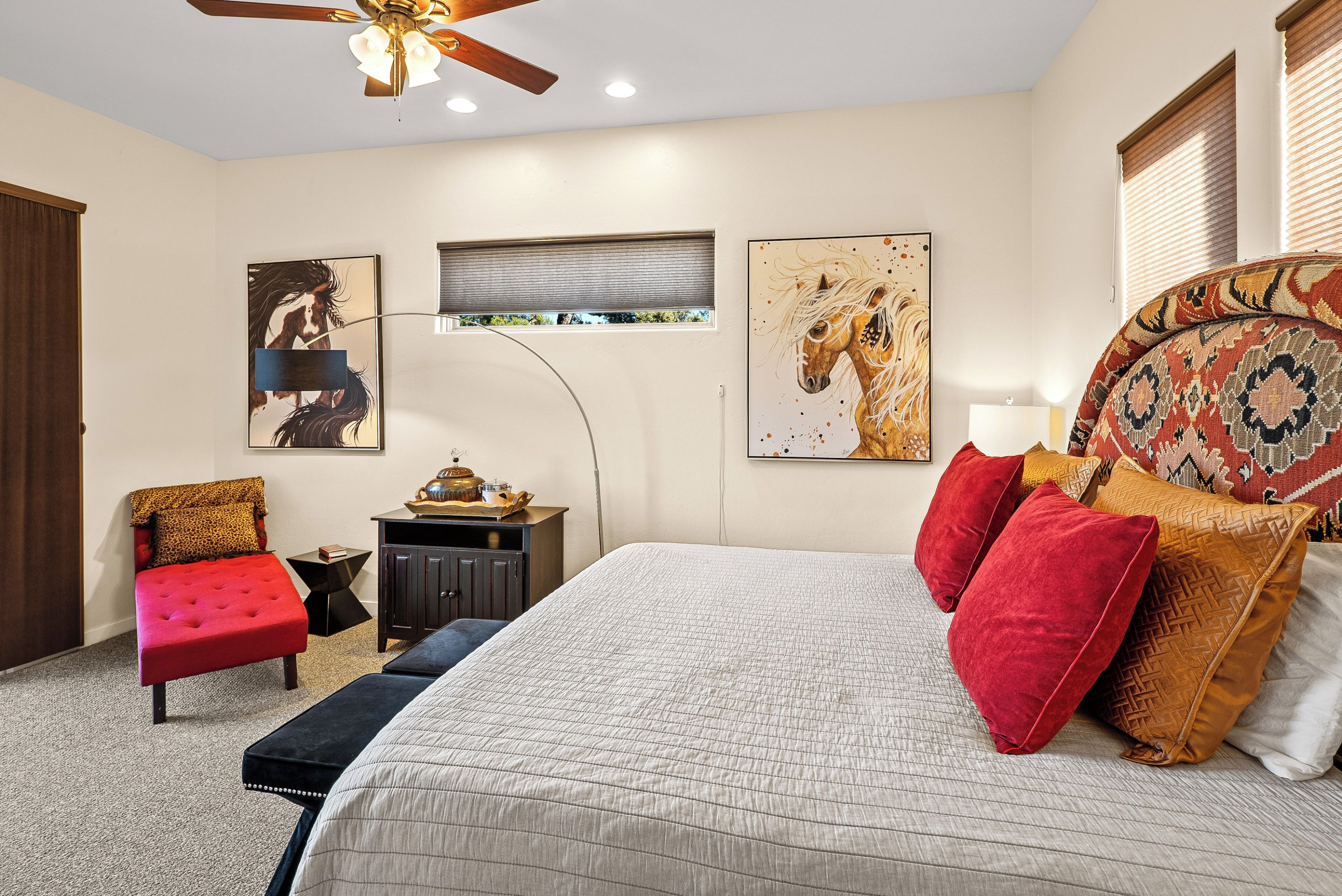 A bedroom with a large bed, a red chair, a small table, and a ceiling fan.