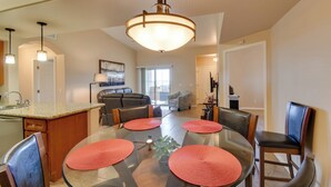 Une cuisine moderne avec un coin repas, comprenant un îlot central, un lustre et une vue sur le salon.