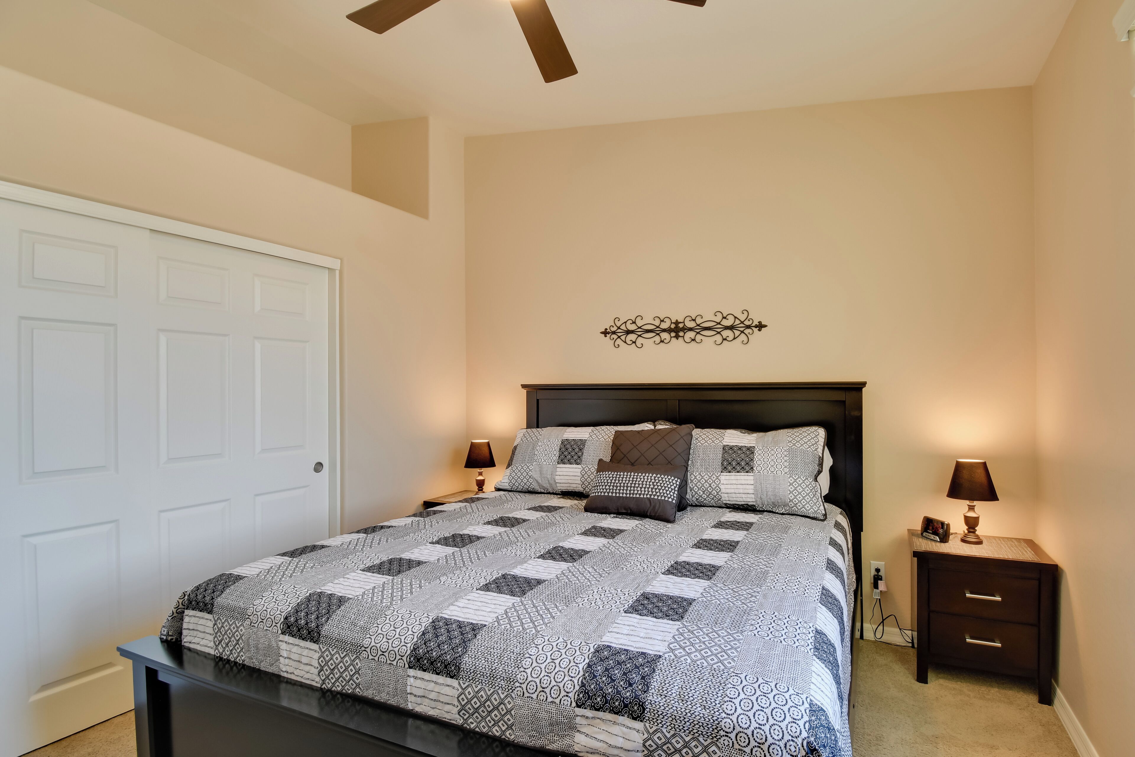 A bedroom with a bed, nightstands, a ceiling fan, and a decorative wall piece.