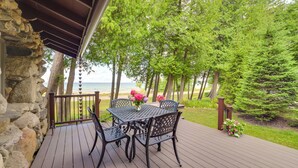 Una terraza de madera con una mesa y sillas, con vista a una playa y árboles.