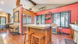 Una cocina con taburetes de madera, una isla grande y vista al océano a través de las ventanas.