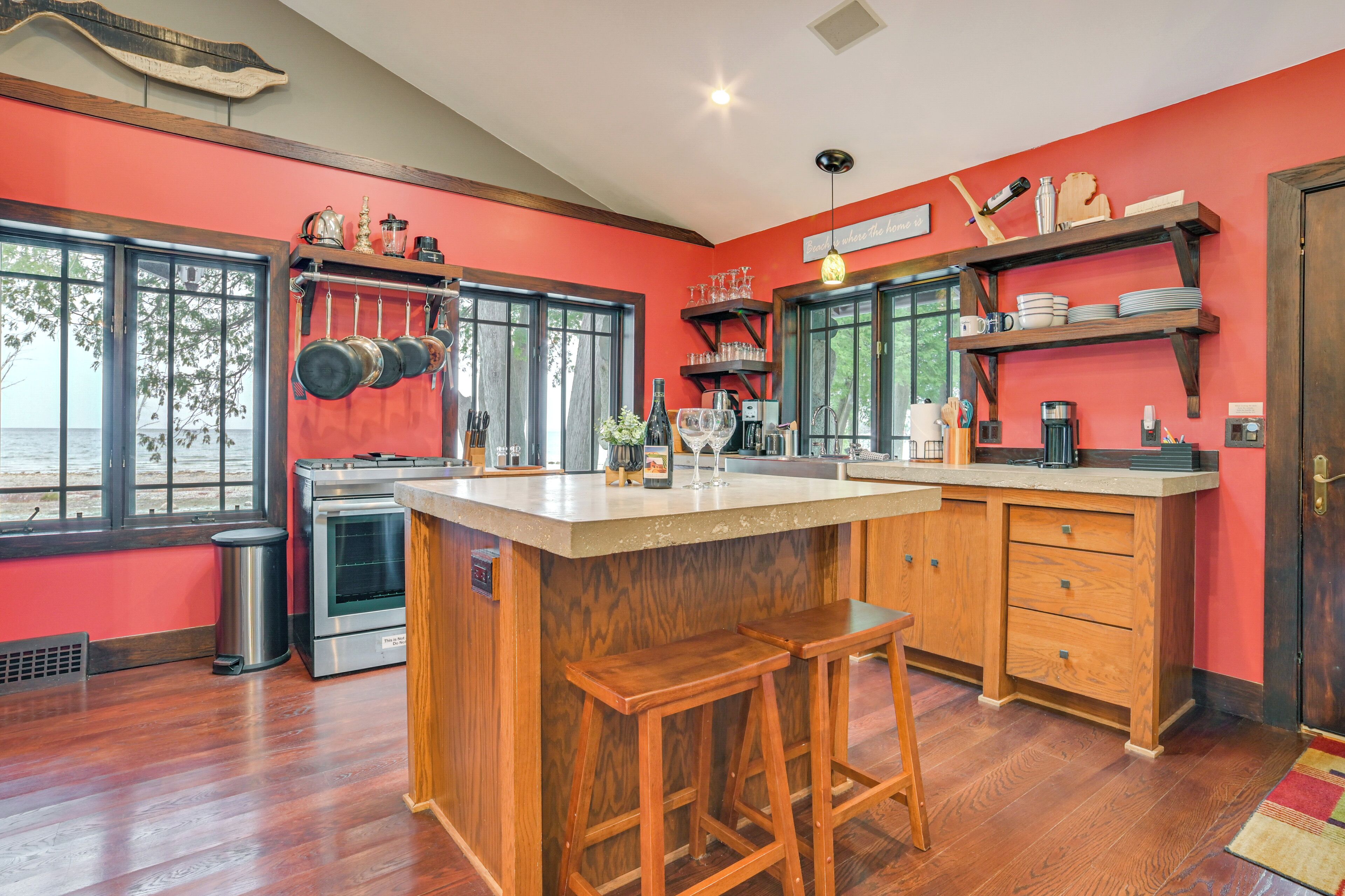 A kitchen with a central island, wooden stools, and a red wall.