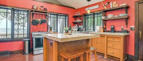A kitchen with a central island, wooden stools, and a red wall.