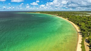 Vista aérea de una zona costera con aguas turquesas cristalinas, una playa de arena y abundante vegetación.