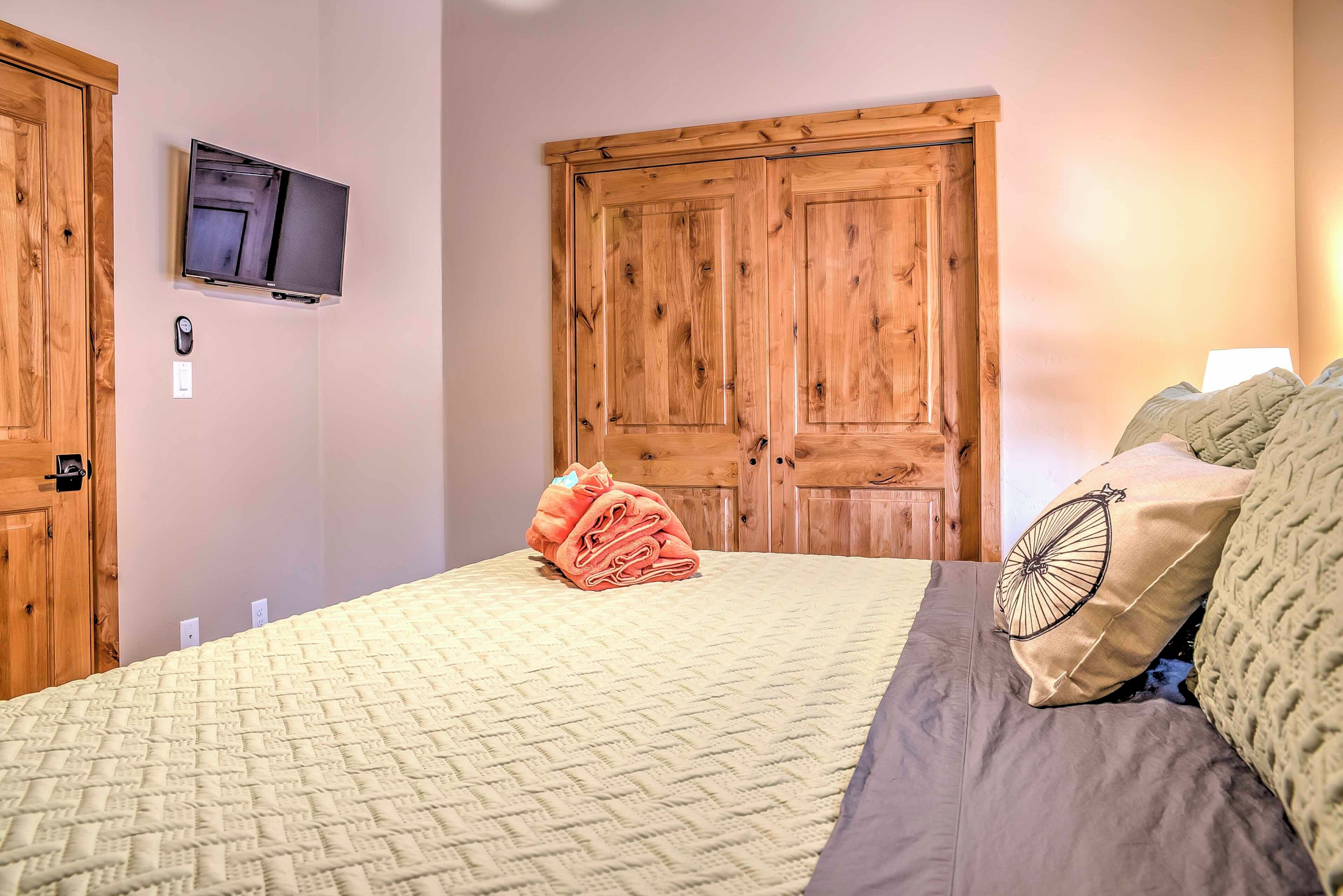 Un dormitorio con una cama, un televisor montado en la pared, puertas de madera y una toalla doblada sobre la cama.
