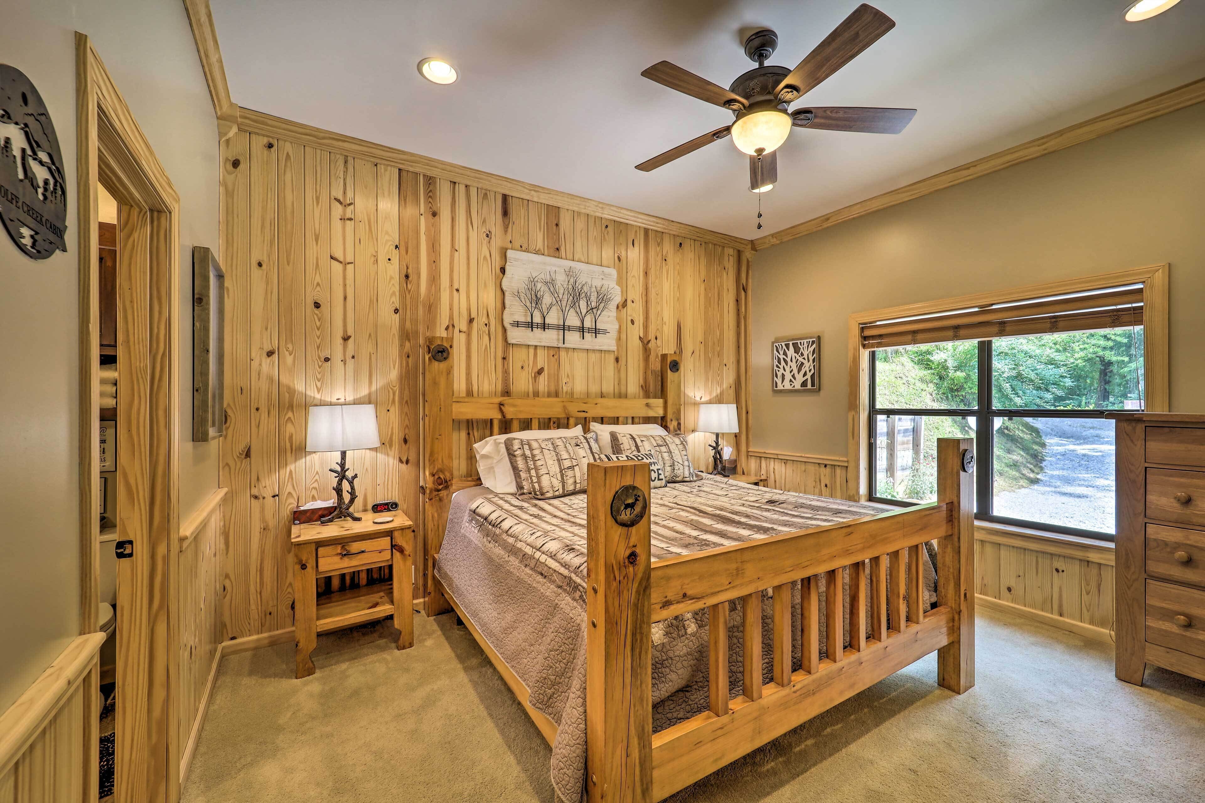 A wooden-paneled bedroom with a bed, bedside tables, a ceiling fan, and a window with a view.