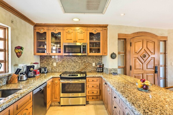 A kitchen with granite countertops, stainless steel appliances, wooden cabinets, and a microwave.