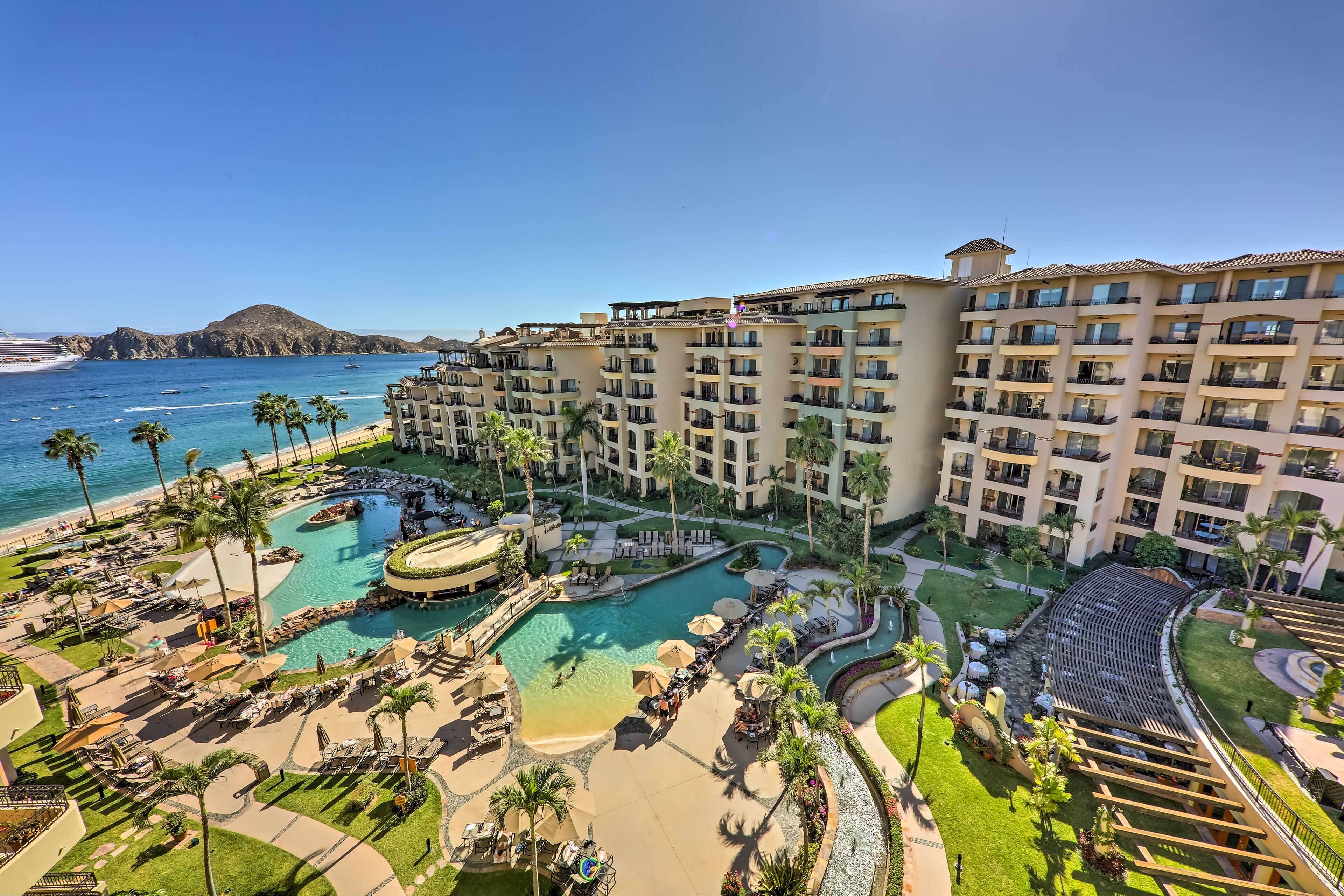 Un resort con una piscina grande, palmeras y vistas al océano.