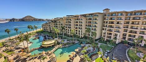 Un resort con una piscina grande, palmeras y vistas al océano.