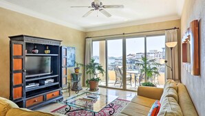 Un salon spacieux doté d’un grand téléviseur, de sièges confortables, d’une table basse en verre et d’un balcon offrant une vue agréable.