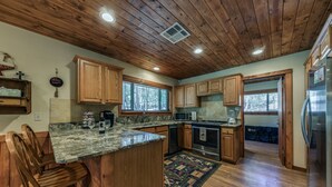 A spacious kitchen with wooden cabinets, a granite countertop, and a central island with seating. - Well-appointed Alto Cabin w/ Fire Pit & Pool Table (Alto)