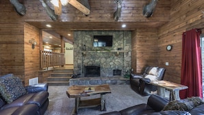 A log cabin interior with a stone fireplace, leather sofas, and a mounted television. - Well-appointed Alto Cabin w/ Fire Pit & Pool Table (Alto)