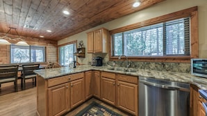 A kitchen with wooden cabinets, granite countertops, a dishwasher, and a window with blinds. - Well-appointed Alto Cabin w/ Fire Pit & Pool Table (Alto)