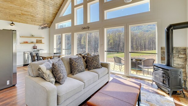 A spacious living area with a high ceiling, large windows, a fireplace, and a cozy seating area. - Modern Appalachian Vacation Rental w/ River Access (Pennington Gap)