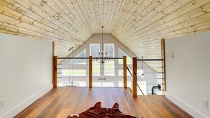A spacious room with a sloped wooden ceiling, a large window, and a chandelier. - Modern Appalachian Vacation Rental w/ River Access (Pennington Gap)
