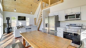 A modern kitchen with white cabinets, stainless steel appliances, and a wooden dining table. - Modern Appalachian Vacation Rental w/ River Access (Pennington Gap)