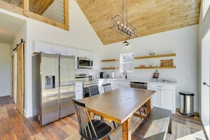 A modern kitchen with white cabinets, stainless steel appliances, and a wooden dining table. - Modern Appalachian Vacation Rental w/ River Access (Pennington Gap)