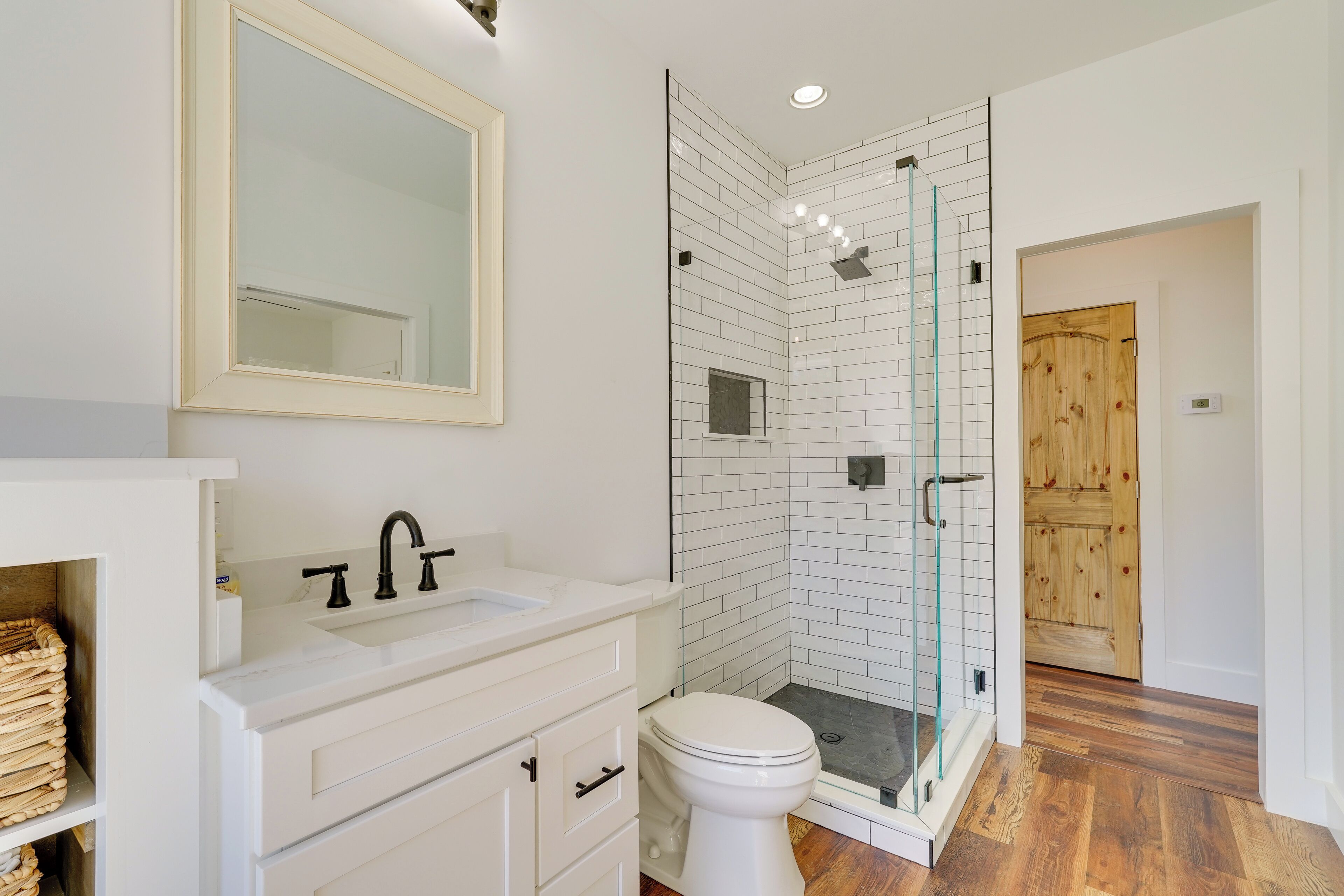 A modern bathroom with a white sink, a mirror, a toilet, and a glass-enclosed shower area.
