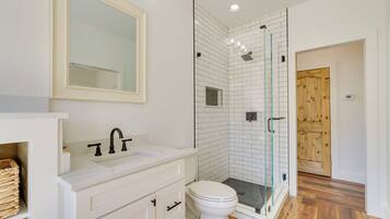 A modern bathroom with a white sink, a mirror, a toilet, and a glass-enclosed shower area.