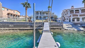 Eine Holzstege führt zu einem Haus mit Pool, umgeben von Palmen und klarem, blauem Wasser.