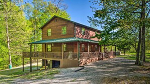 Eine zweistöckige Blockhütte mit Veranda und einer Terrasse, umgeben von Bäumen.
