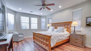 Une chambre à coucher avec un lit en bois, deux tables de chevet avec des lampes, un bureau avec une chaise et de grandes fenêtres équipées de stores.