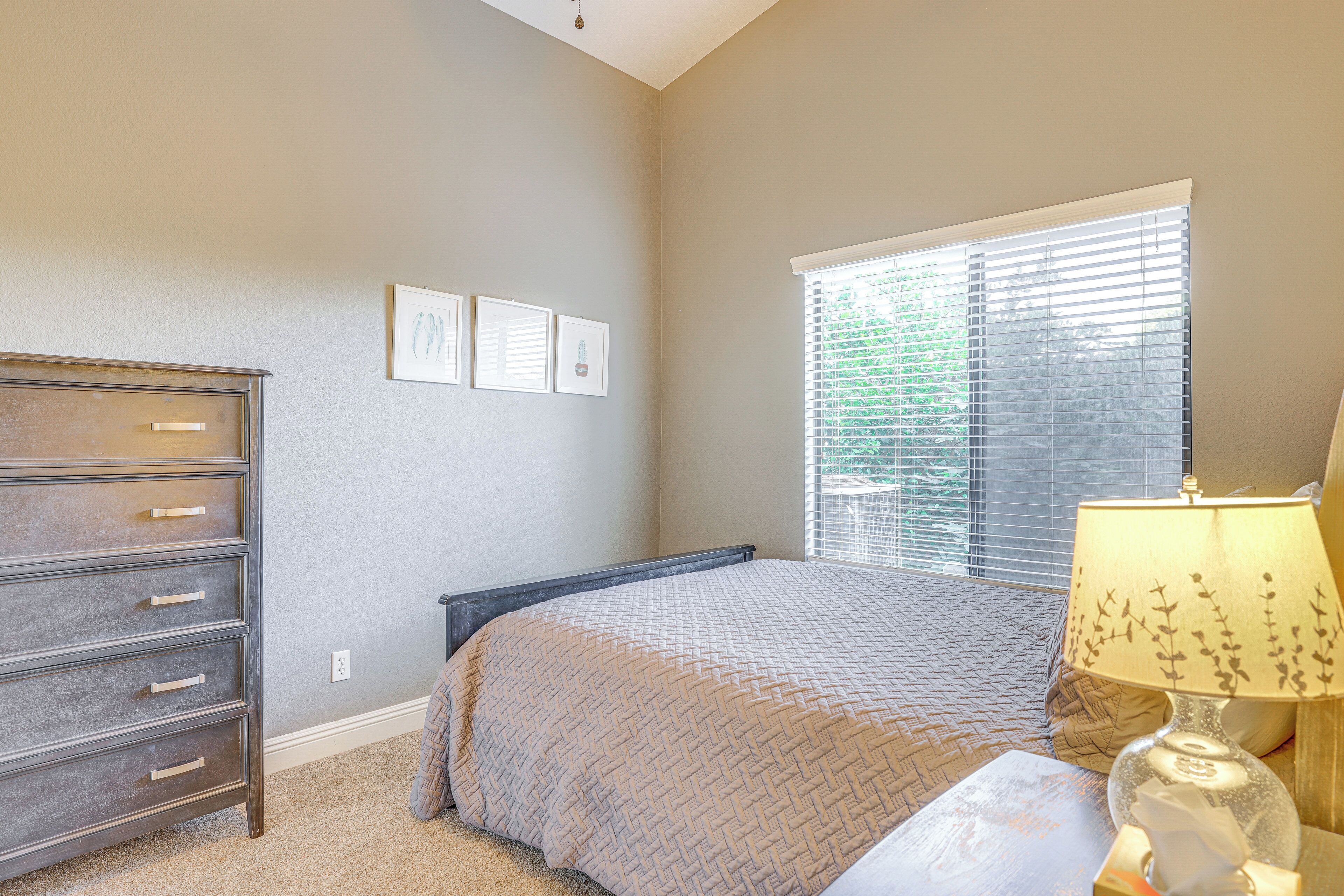 A bedroom with a bed, dresser, window with blinds, and a lamp.