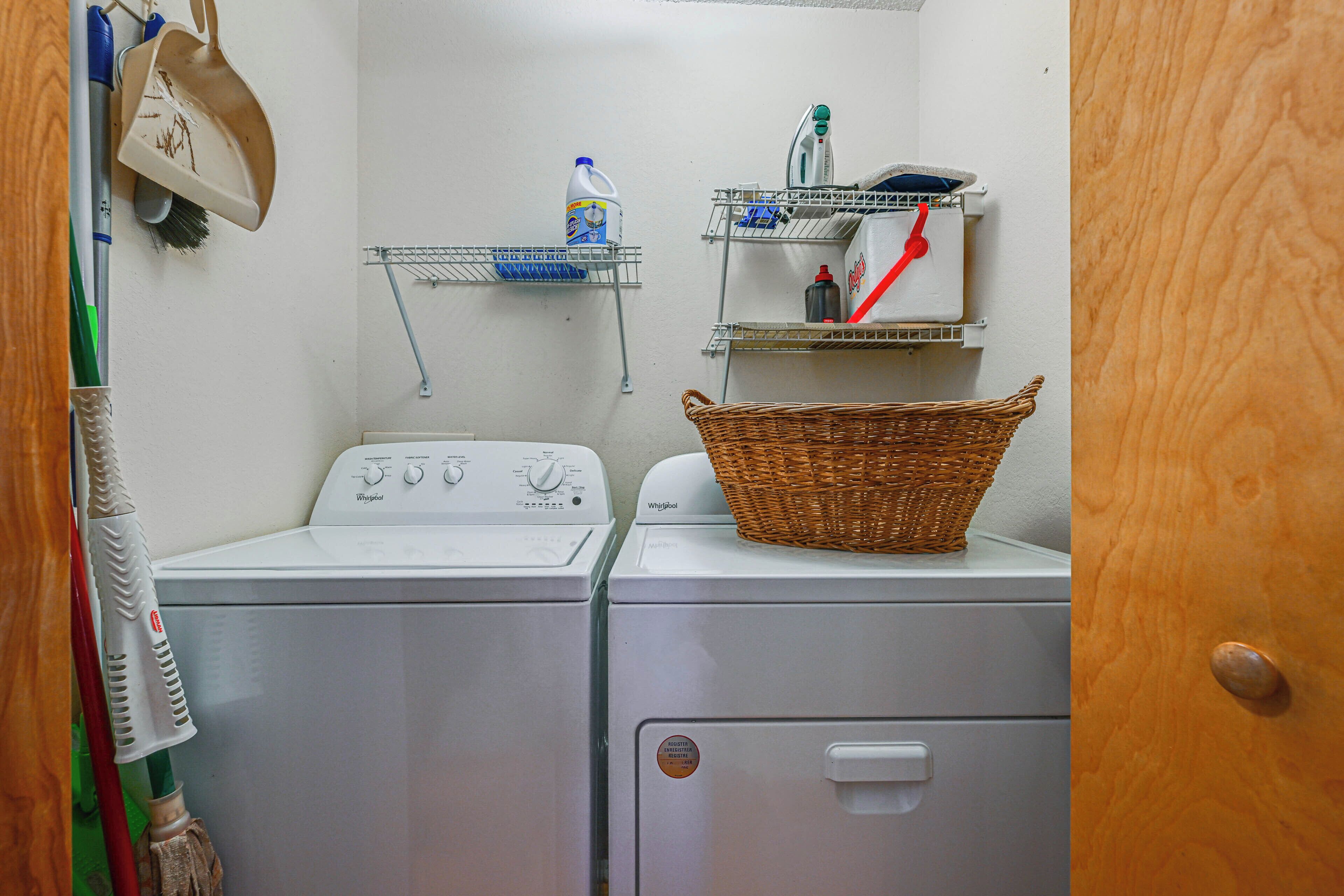 A laundry area with two washing machines, a basket, and shelves with cleaning supplies.