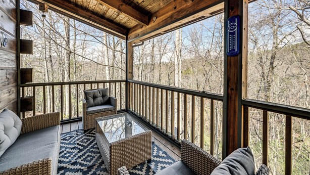 A wooden deck with wicker furniture and a glass table, overlooking a forested area. - Bryson City Cabin w/ Hot Tub, Views & Pool Table! (Bryson City)