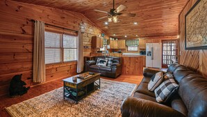 A cozy cabin interior with a wooden ceiling, a ceiling fan, a living room with a sofa and coffee table, a kitchen area, and a dining table. - Bryson City Cabin w/ Hot Tub, Views & Pool Table! (Bryson City)