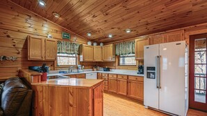 A wooden cabin interior with a kitchen featuring wooden cabinets, a refrigerator, a sink, and a dining area with a table and chairs. - Bryson City Cabin w/ Hot Tub, Views & Pool Table! (Bryson City)