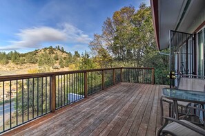 A wooden deck with a glass table and chairs, overlooking a hilly landscape with trees and a road. - Lake View Home w/ Grill: Hike, Boat, Relax! (Kelseyville)