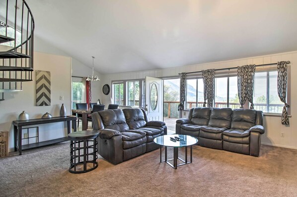 A spacious living room with a large sectional sofa, a coffee table, and a dining area with a table and chairs. A spiral staircase is visible in the background. - Lake View Home w/ Grill: Hike, Boat, Relax! (Kelseyville)