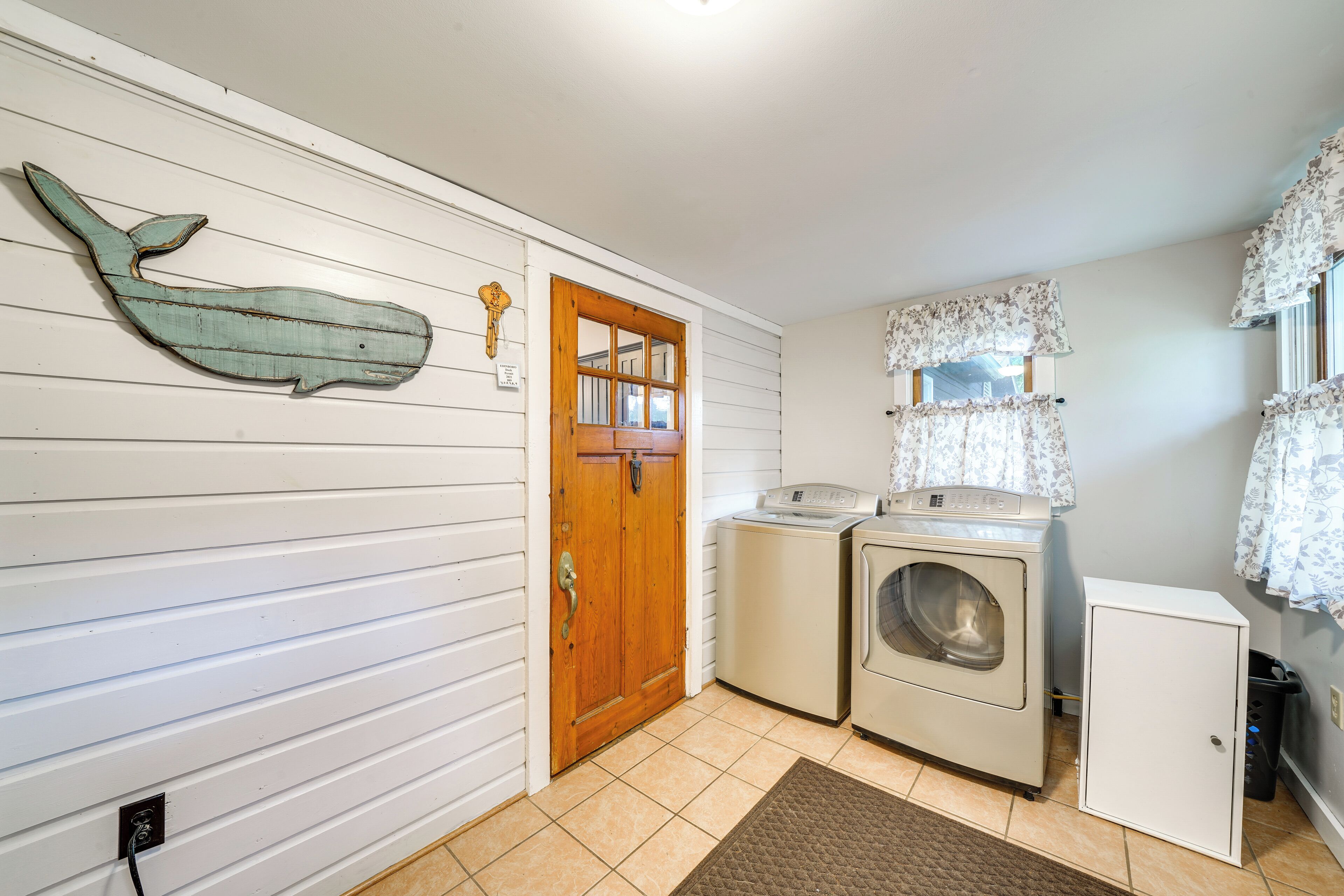 A laundry room with a wooden door, a washing machine, a dryer, and a small cabinet.