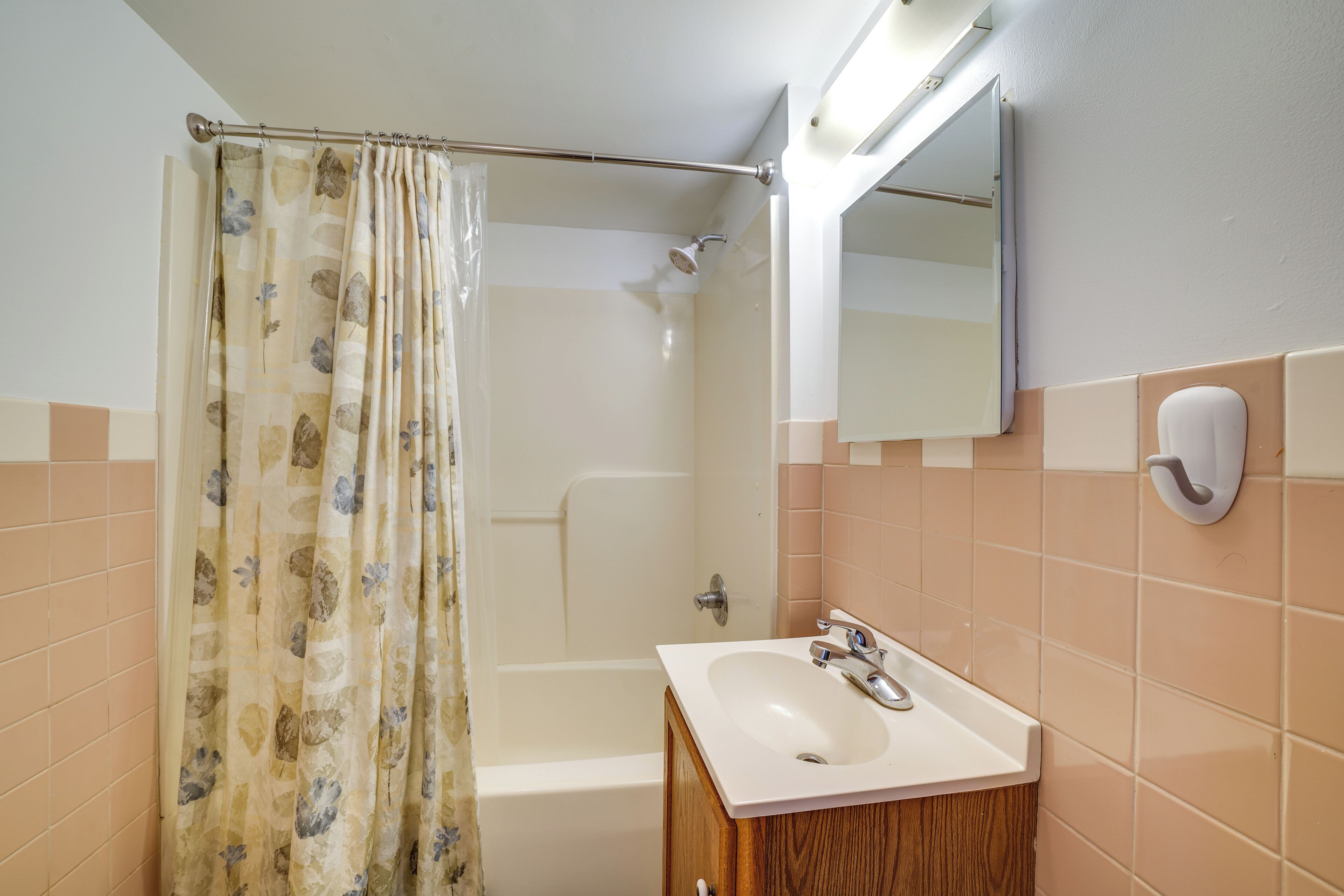 A bathroom with a shower curtain, a bathtub, a sink, and a mirror.