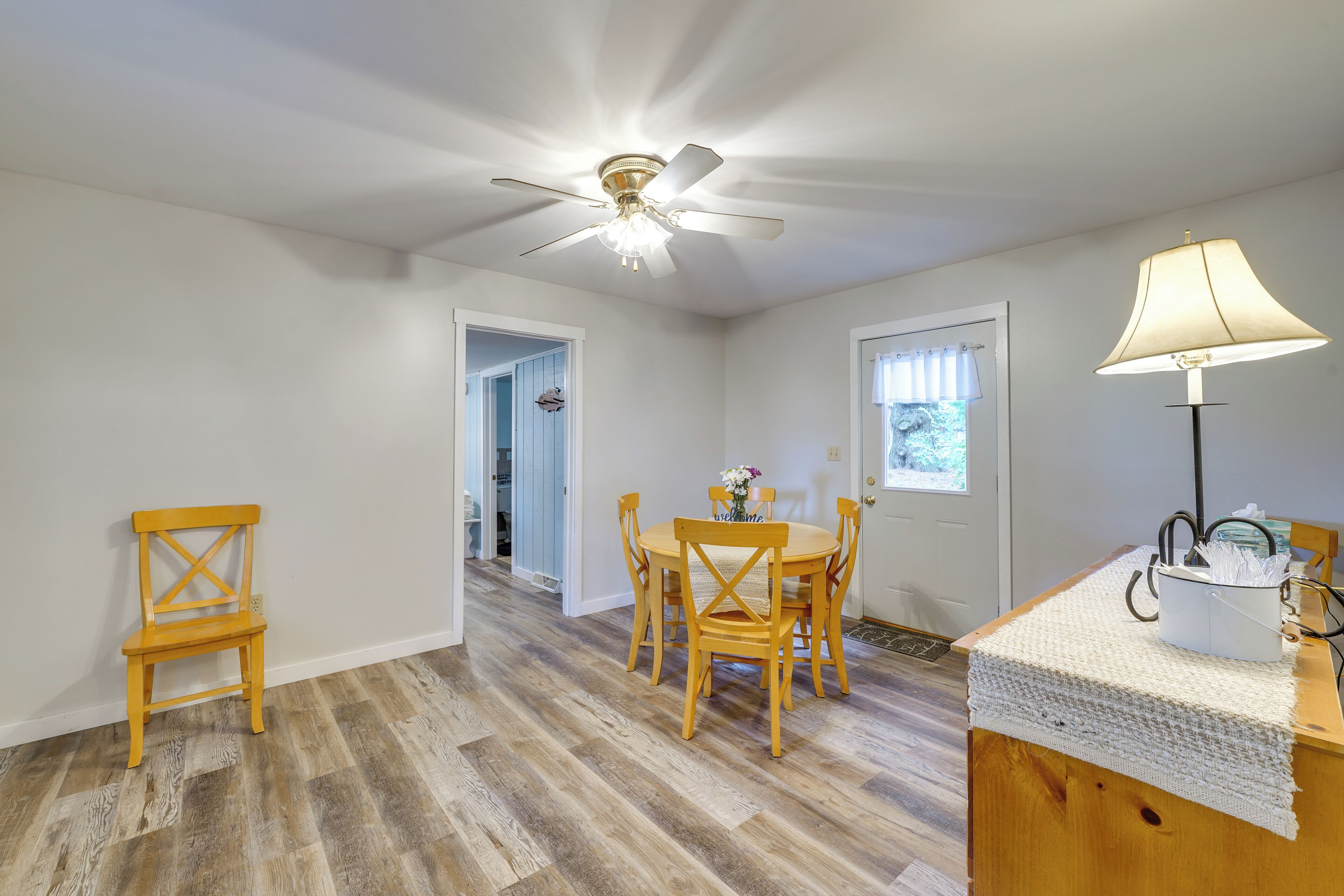A room with a dining table, chairs, a ceiling fan, and a lamp.