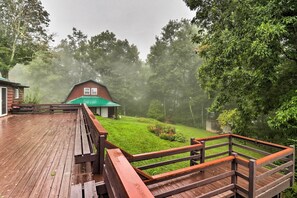 Une terrasse en bois avec une rambarde en bois, une pelouse verdoyante et, au fond, un bâtiment rouge surmonté d’un toit vert.
