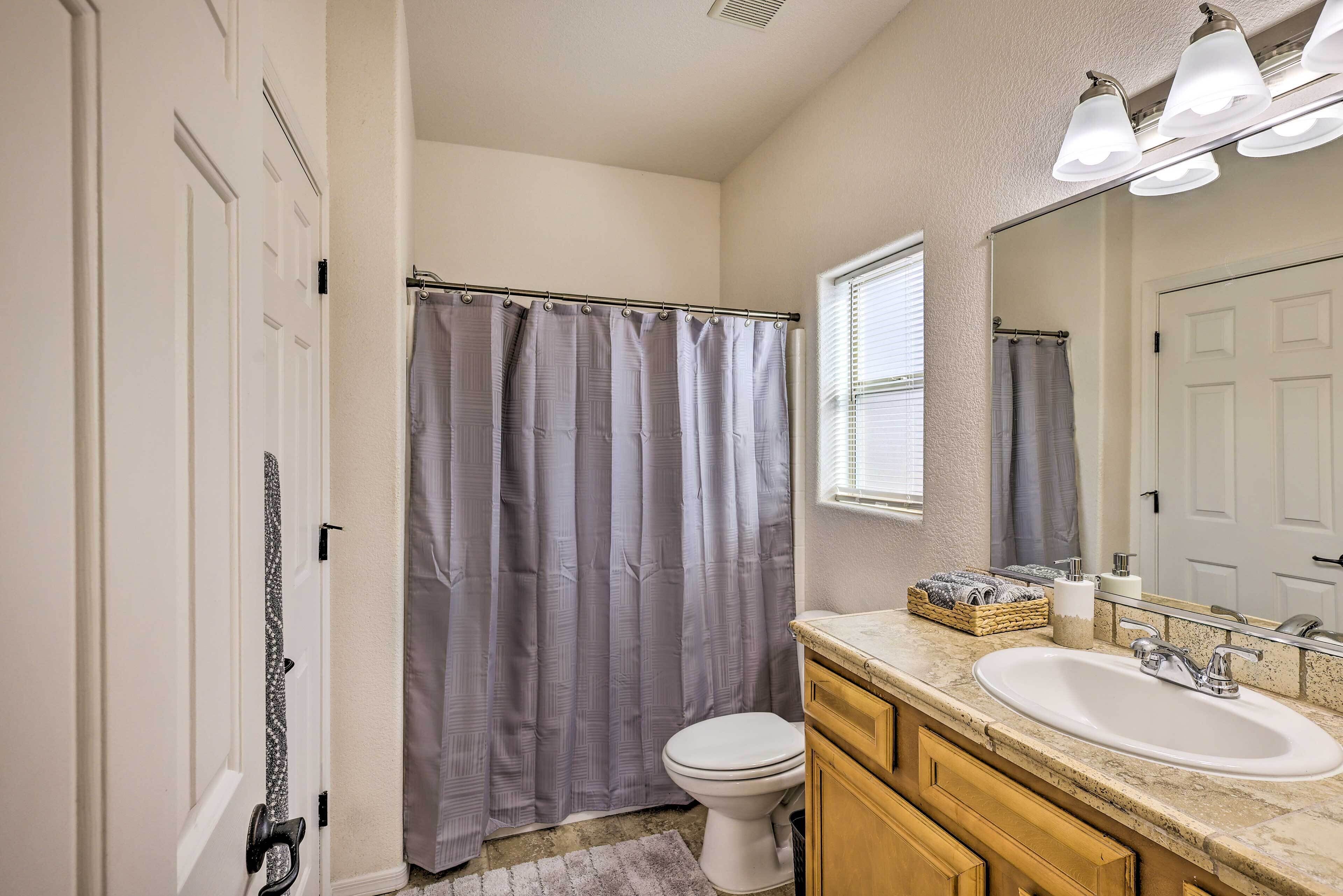 A bathroom with a shower curtain, toilet, sink, and mirror.