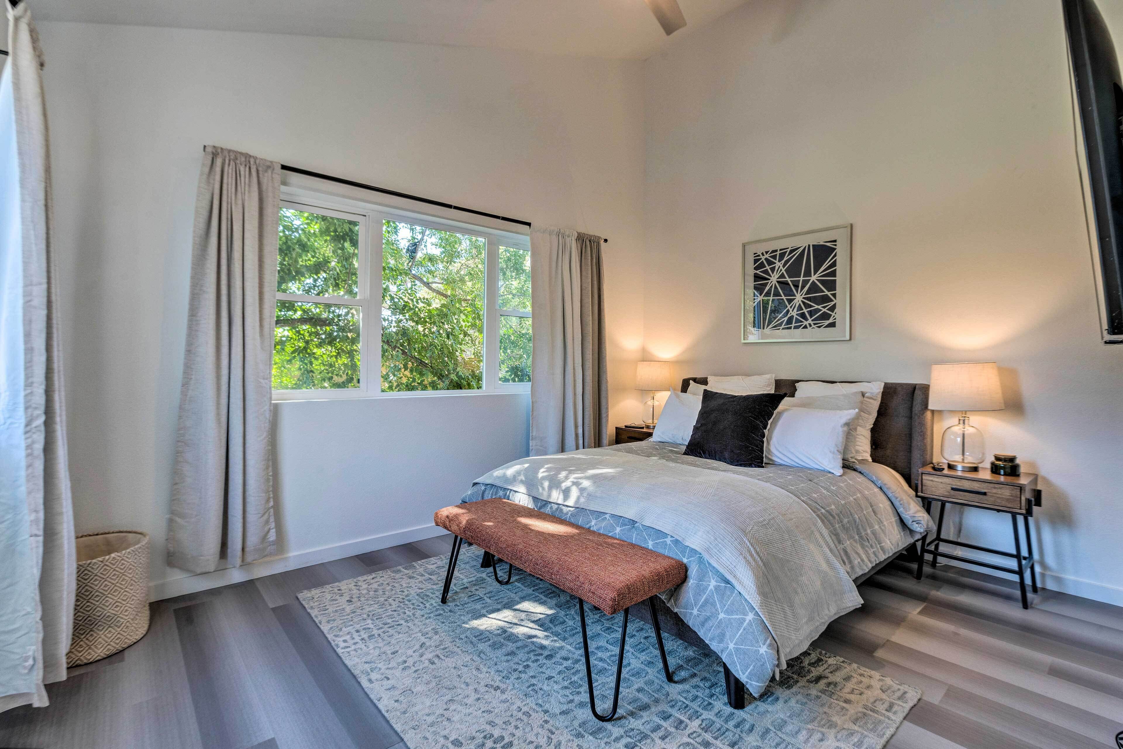 A bedroom with a bed, bedside tables, a bench, a rug, and a window with curtains.