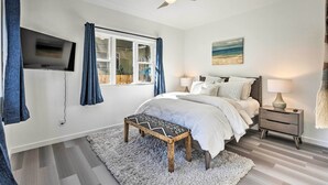 A bedroom with a bed, bedside tables, a TV mounted on the wall, a ceiling fan, and a window with curtains. - Modern Midtown Haven w/ Garage: Mt Rose Day Trips! (Reno)