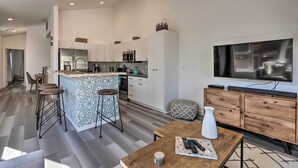 A modern kitchen with white cabinets, a central island with stools, a microwave, and a large flat-screen TV mounted on the wall. - Modern Midtown Haven w/ Garage: Mt Rose Day Trips! (Reno)