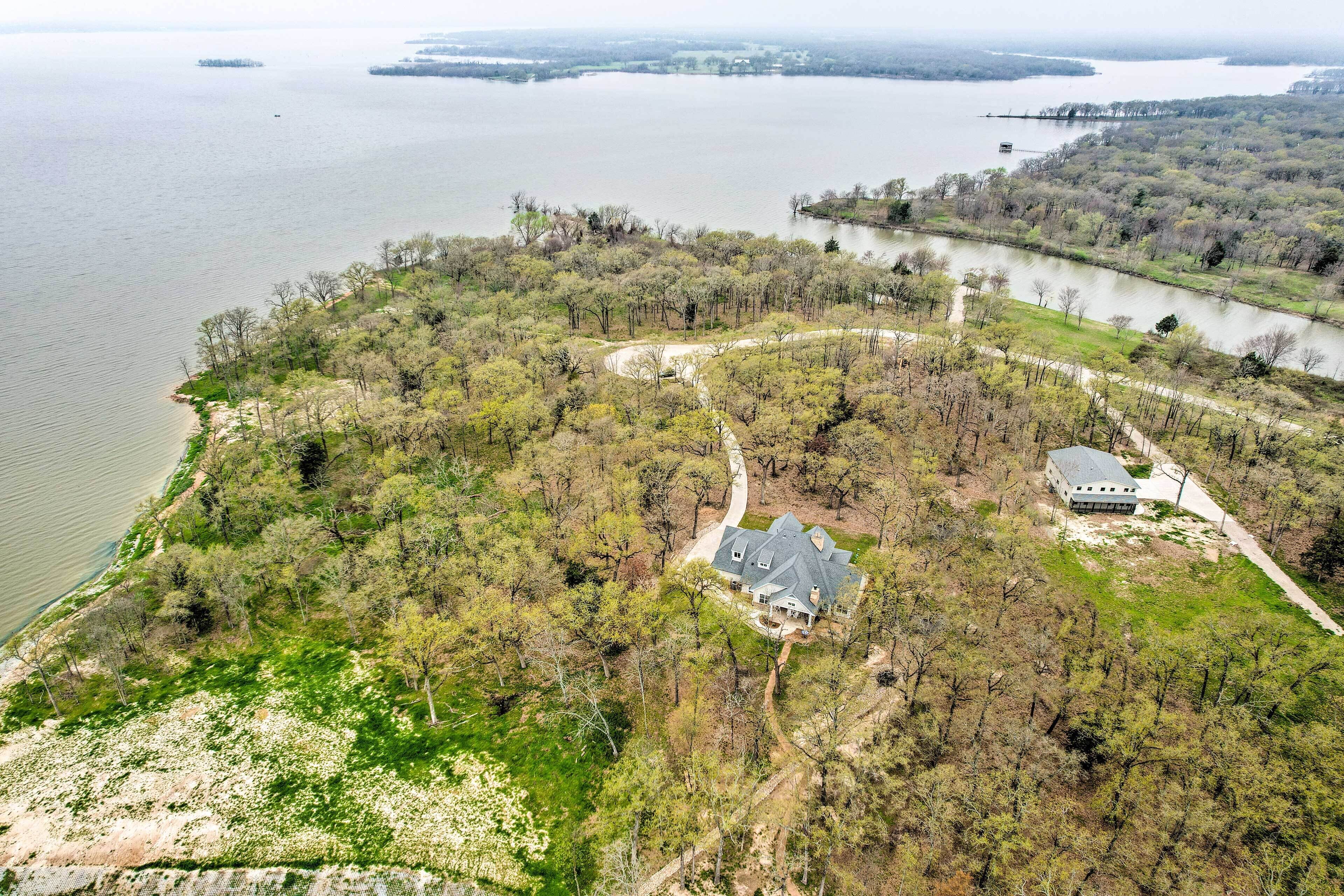 An aerial view of a property with a house surrounded by dense trees, a lake, and a winding road.