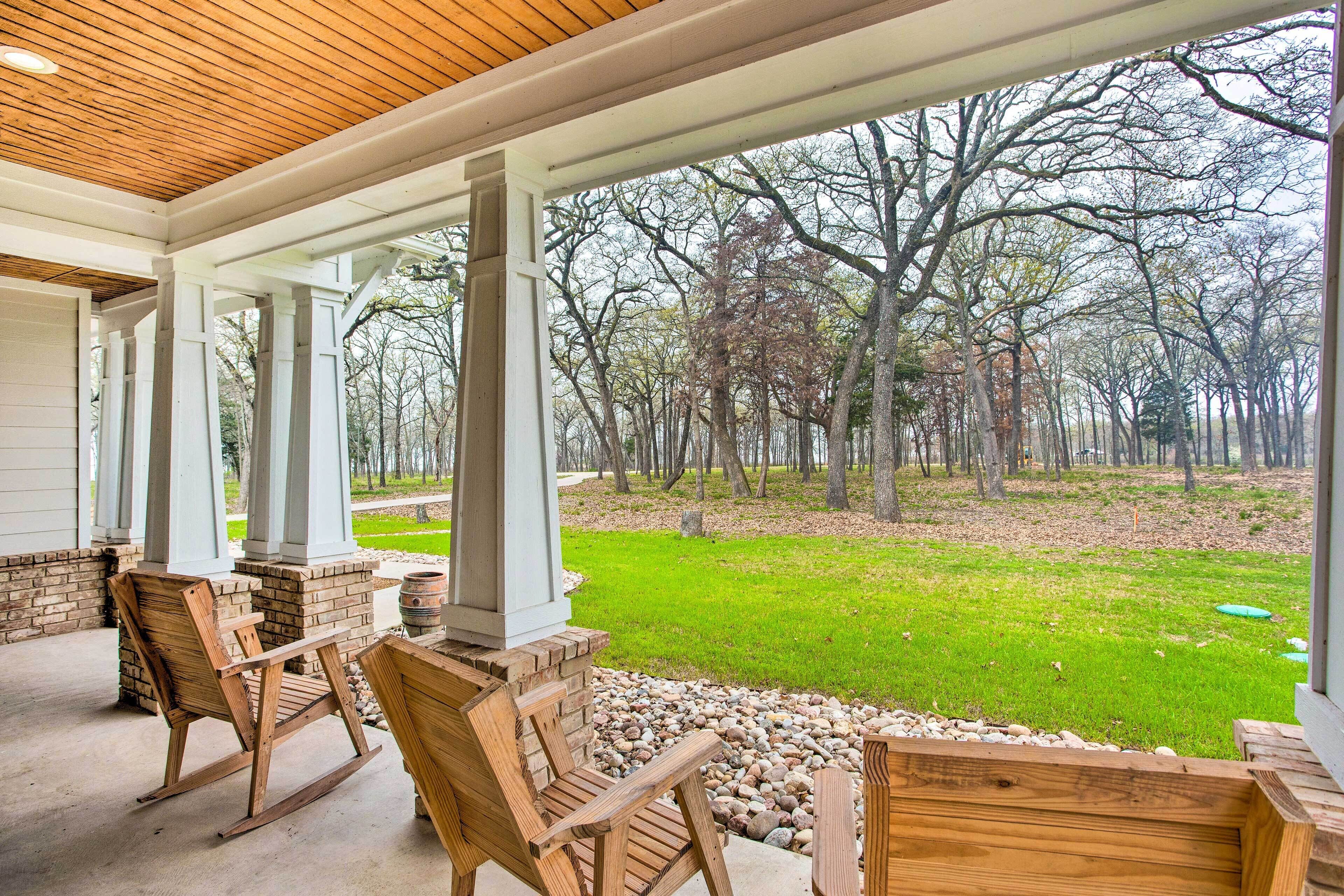 A covered patio with wooden rocking chairs and a view of a wooded area.