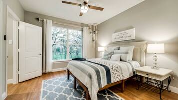 A bedroom with a bed, bedside tables, a ceiling fan, a window with curtains, and a motivational quote on the wall.