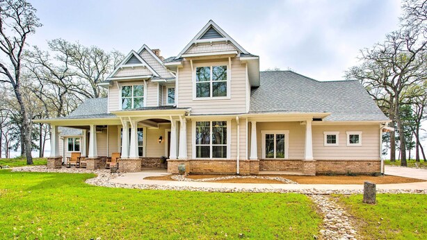 A two-story house with a large front porch, a covered entryway, and a stone foundation. - Waterfront Lake Tawakoni Home w/ Fire Pit! (Quinlan)