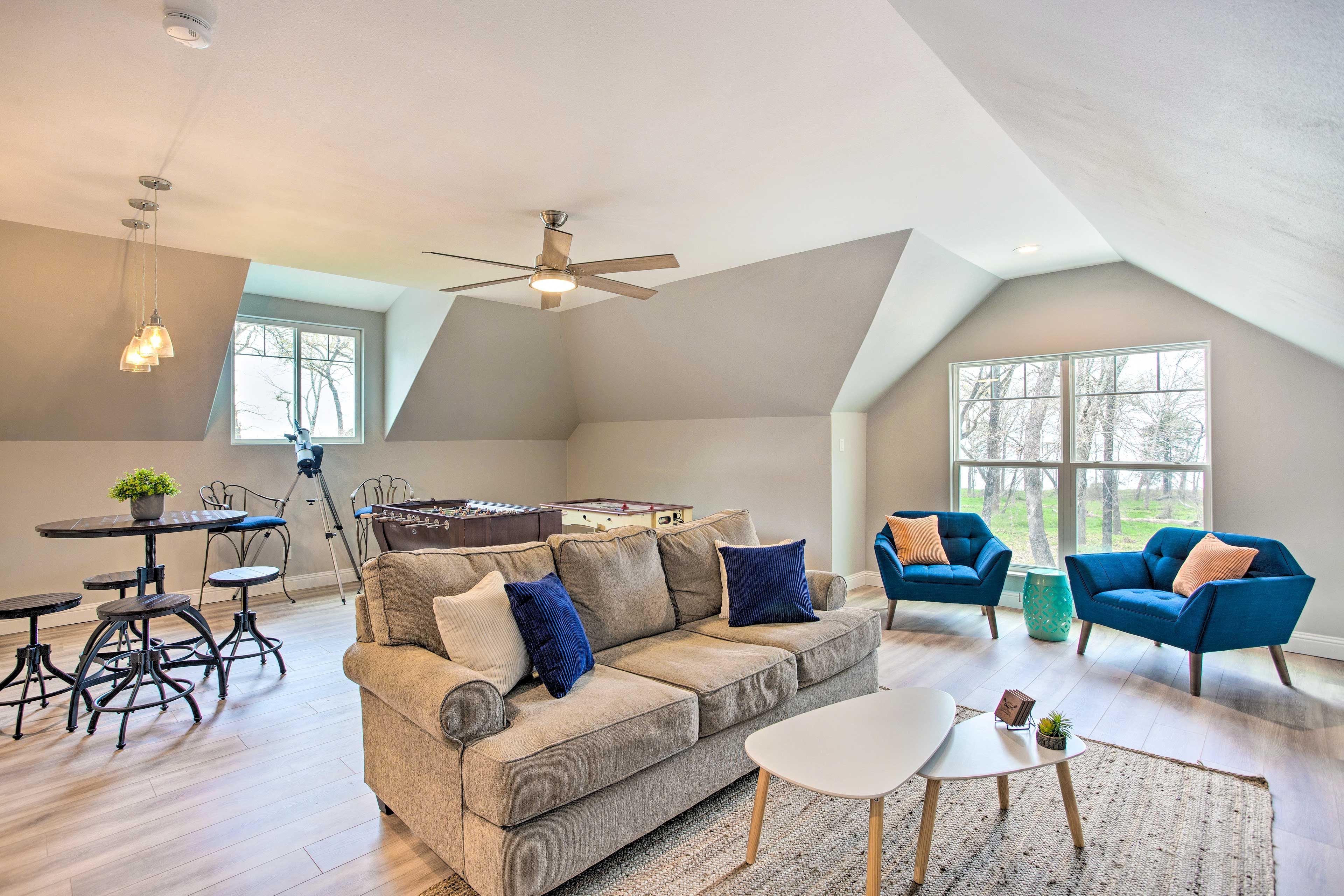 A spacious loft with a high ceiling, a large window, a sofa, two armchairs, a coffee table, and a dining area with a table and chairs.